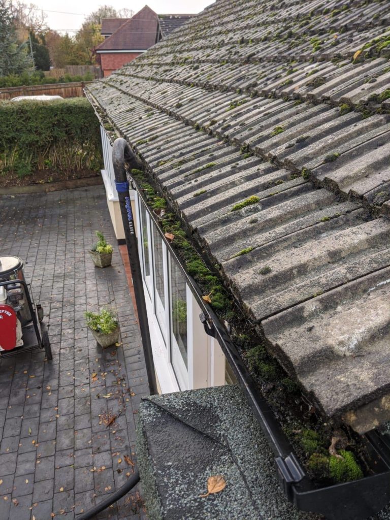 Before gutter cleaning - blocked gutters filled with leaves, moss and debris causing water overflow